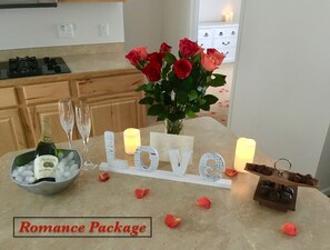 A table with a 'Romance Package' sign, a bottle of champagne, two glasses, a vase of roses, candles, and a chocolate tray. - Best Views in Anchorage! Totally Private, Romantic, and Family Friendly Suite! (Anchorage)