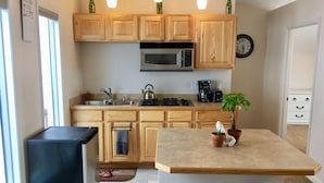 A kitchen with wooden cabinets, a microwave, a kettle, and a coffee maker. There are two stools and a potted plant on the island. - Best Views in Anchorage! Totally Private, Romantic, and Family Friendly Suite! (Anchorage)