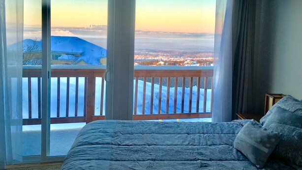 A bedroom with a large bed, a view through a sliding glass door to a balcony with a wooden railing, and a snowy landscape outside. - Best Views in Anchorage! Totally Private, Romantic, and Family Friendly Suite! (Anchorage)