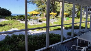Un espace extérieur aménagé, abrité et doté de tables et de chaises, offrant une vue sur une plage parsemée de parasols et de chaises longues.