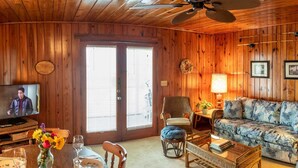 L’intérieur d’un chalet en bois accueillant, doté d’un téléviseur, d’un canapé, d’une table à manger et d’un ventilateur de plafond.