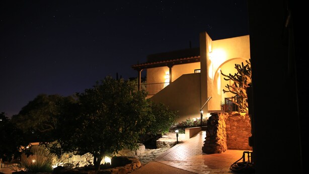 A nighttime view of a building with a stone pathway leading to a lighted entrance. - Magical Private Mountain Estate in Ventana Canyon  (Tucson)