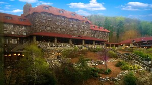 A large stone building with multiple levels and red roofs, surrounded by a landscaped garden with pathways and outdoor seating areas.