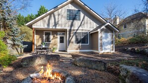 A two-story house with a front porch, a fire pit, and a small patio area.