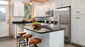 A modern kitchen with white cabinets, stainless steel appliances, a large island with stools, and pendant lighting.
