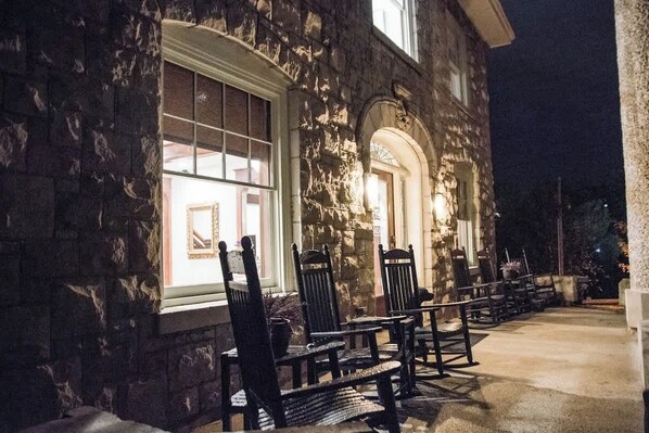 A stone building with a porch, outdoor seating, and a well-lit entrance.