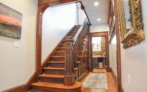 A wooden staircase with a handrail, a rug on the floor, and a painting on the wall. - The Stone House at Black Dog Salvage (Roanoke)