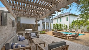 Ein überdachter Außenbereich mit Grill, Sitzgelegenheiten und Pool.