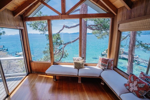 A wooden interior with a bench and large windows overlooking a body of water.