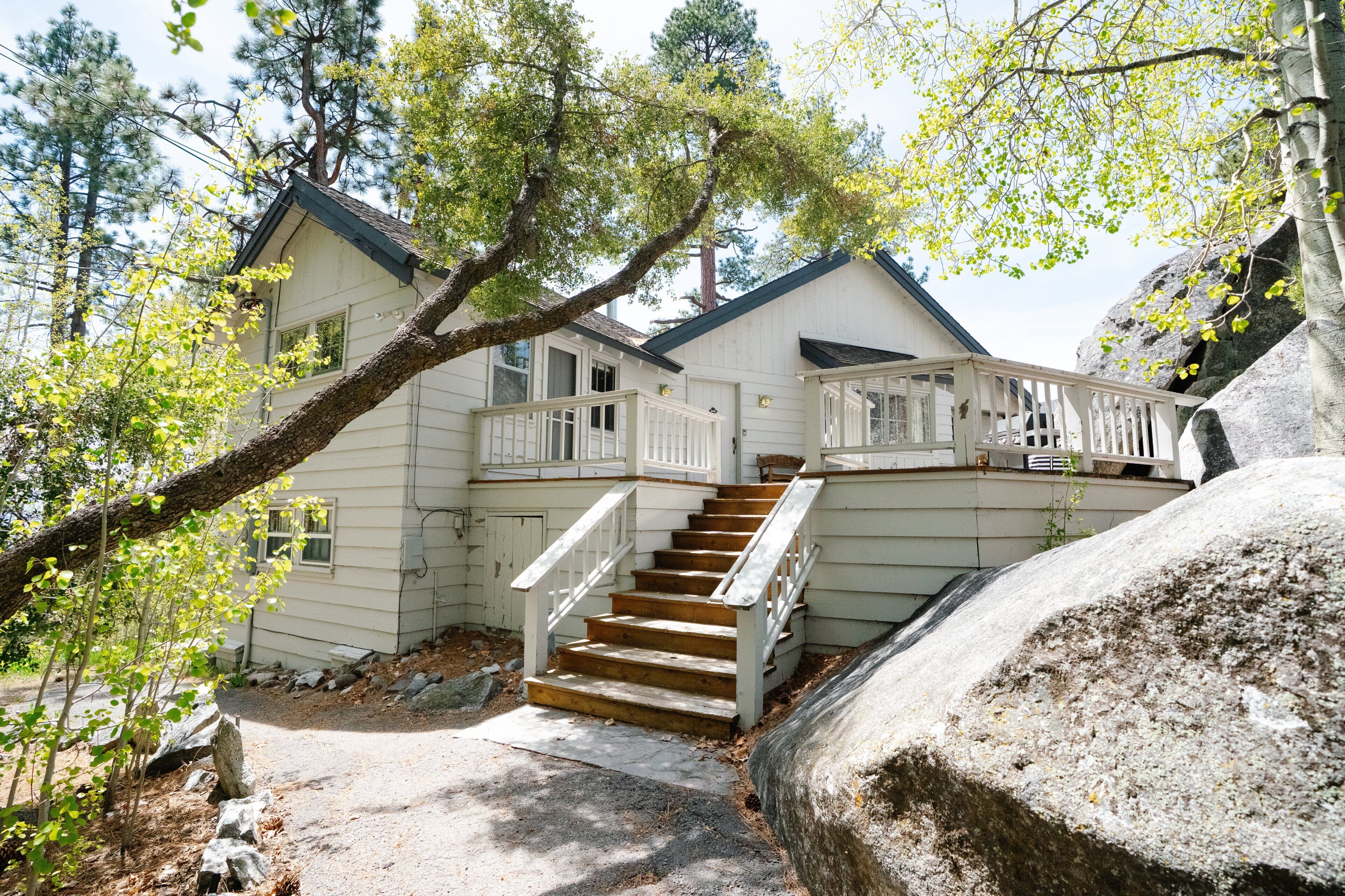 A house with a wooden staircase leading to a porch, surrounded by trees and rocks.