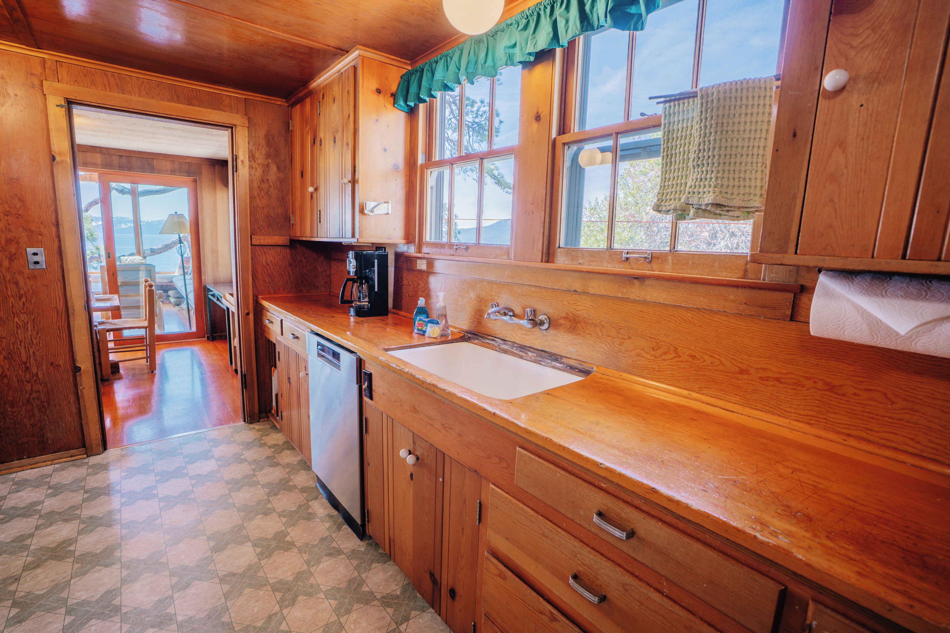 Una cocina de madera con un lavamanos, armarios y vistas al exterior.