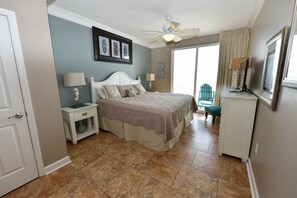 A bedroom with a bed, nightstands, a ceiling fan, and a view of the outside.