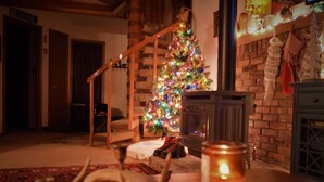 A cozy living room with a wooden staircase, a decorated Christmas tree, a fireplace, and a candle on a table. - Whitefish Mountain Resort, Ski In Ski Out Condo, 3 Bed 2 Bath, Private Hot Tub! (Whitefish)