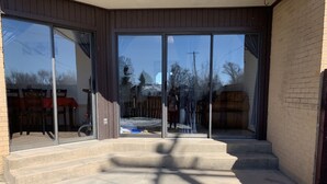 A concrete staircase leading to a glass door entrance with a view of a snowy backyard and a red tablecloth visible through the glass.