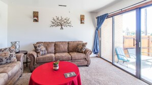 A living room with a brown leather sofa, a red table, and a large sliding glass door leading to an outdoor patio.