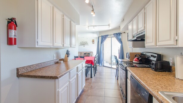 A kitchen with white cabinets, a granite countertop, a red table, and a fire extinguisher.
