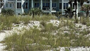 En fastighet vid stranden med ett stort hus i flera våningar, som har en central balkong och många fönster.