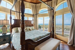 Een hemelbed met uitzicht op het strand door grote ramen.
