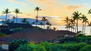 A coastal property with a large house, lush greenery, and a view of the ocean at sunset. - A403 - Spacious 1 Bedroom, 2 King Bed, Garden and Partial Ocean Views (Lahaina)