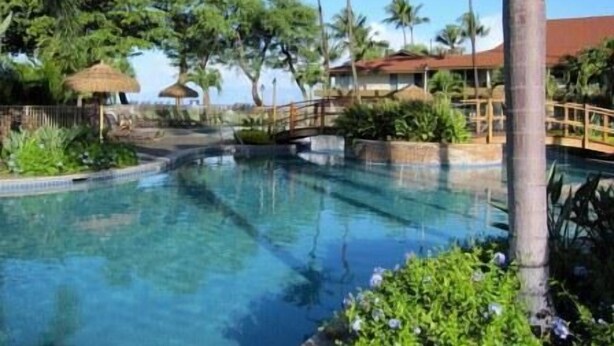 A clear swimming pool surrounded by tropical vegetation and a wooden bridge. - A403 - Spacious 1 Bedroom, 2 King Bed, Garden and Partial Ocean Views (Lahaina)