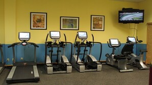 Ein Fitnessraum mit Laufbändern, Crosstrainern und einem Fernseher, der ein Rennen zeigt.