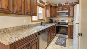 Una cocina con encimeras de granito, armarios de madera y electrodomésticos de acero inoxidable, además de un ventanal.