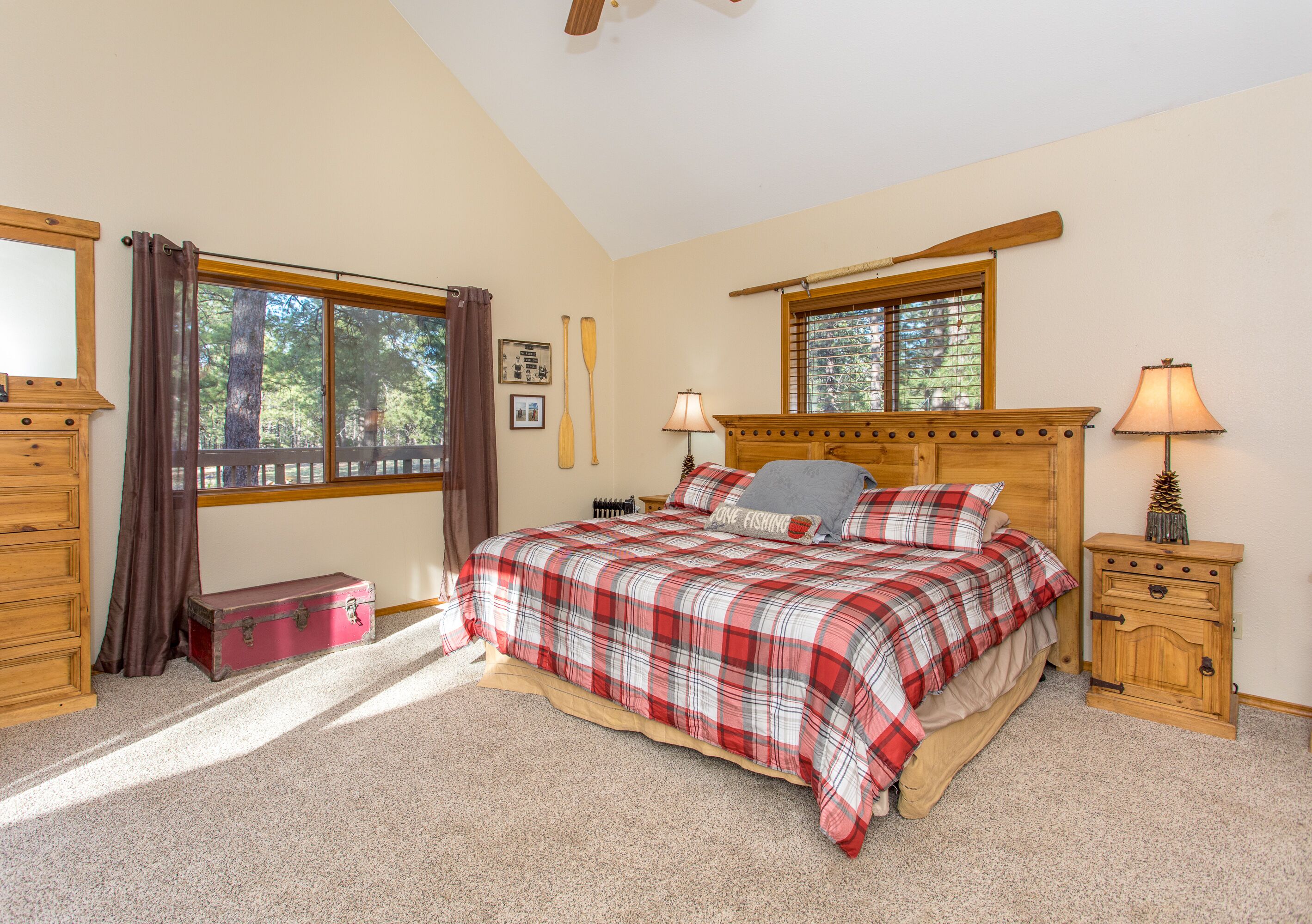 A bedroom with a bed, wooden headboard, two bedside tables, a nightstand, a window with curtains, a dresser, and a suitcase.