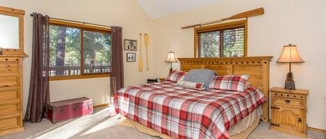 A bedroom with a bed, wooden headboard, two bedside tables, a nightstand, a window with curtains, a dresser, and a suitcase.