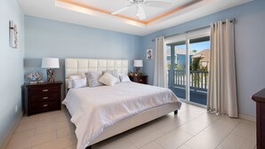 A bedroom with a bed, nightstands, a ceiling fan, and a view of the outside. - Modern Beach House • Heated Pool • 3 Min Walk to Beach (South Padre Island)