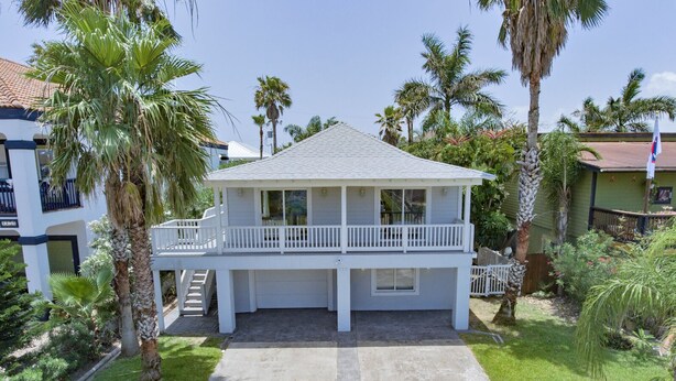 A two-story house with a balcony, surrounded by palm trees and a well-maintained lawn. - Modern Beach House • Heated Pool • 3 Min Walk to Beach (South Padre Island)
