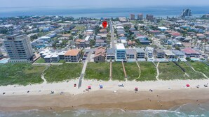 An aerial view of a coastal town with a beach, buildings, and a marked location. - Modern Beach House • Heated Pool • 3 Min Walk to Beach (South Padre Island)