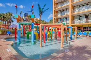A water play area with colorful structures and a pool, surrounded by a multi-story building with balconies. - WOW SWING/ INDOOR/OUTDOOR LIVING/KING/300SQFT SUNDECK TERRACE/FIREPLACE//SLEEP4 (Myrtle Beach)