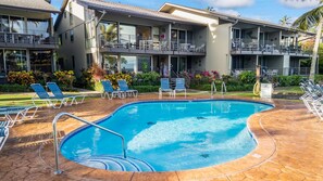 A swimming pool with lounge chairs and a building with balconies.