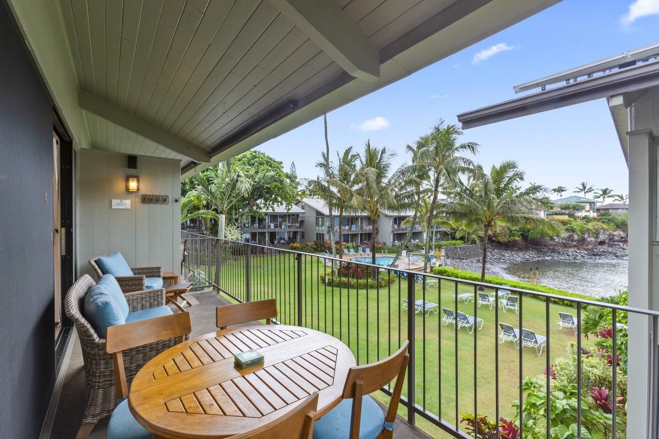Your private lanai at #217, with seating, a dining table, and views across the shared grounds to the cove.