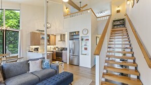 En rummelig opholdsstue med sofa, skammel og trappe til et højere plan.