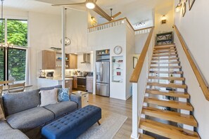 Un vaste espace de vie comprenant un canapé, un pouf et un escalier menant à un niveau supérieur.