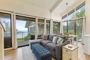A spacious living room with a large gray sectional sofa, a blue ottoman, and a dining area with a table and chairs.