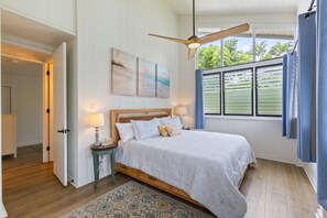 A bedroom with a bed, a ceiling fan, a window with curtains, and a painting on the wall.