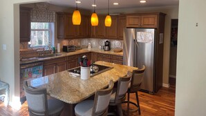 A modern kitchen with granite countertops, wooden cabinets, a stainless steel refrigerator, and pendant lighting. - Mountain House at the Beach! Dog Friendly, Short Walk to the Beach. (Villas)
