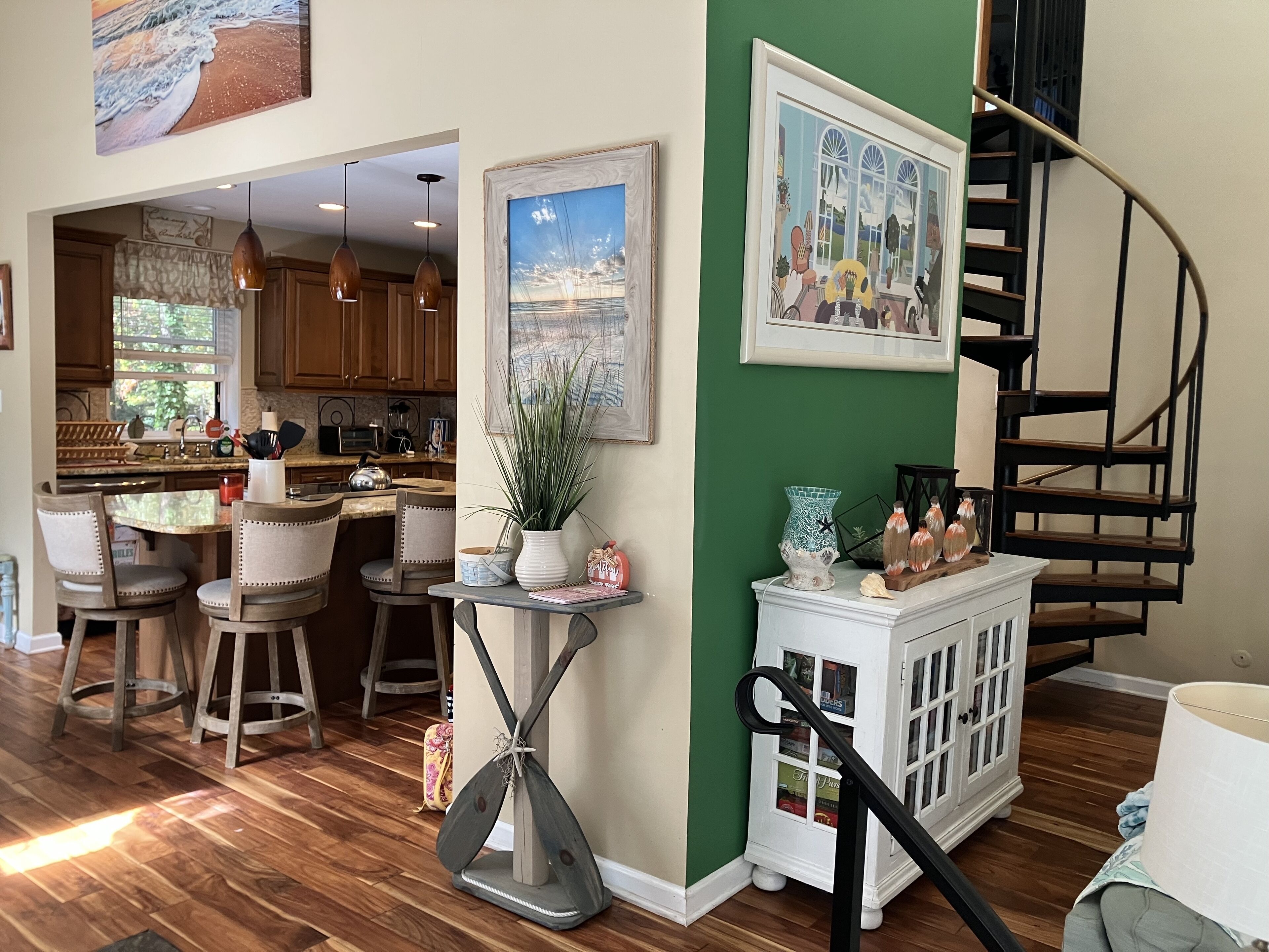 A modern kitchen with wooden cabinets, a dining area with bar stools, a staircase, and a view of the outdoors.