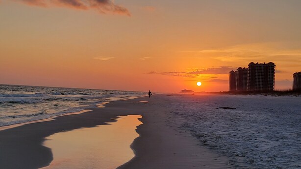 Ein Strand bei Sonnenuntergang, eine Person geht im Sand entlang.