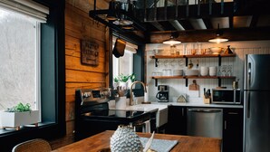 A modern kitchen with wooden accents, stainless steel appliances, and a dining area with a wooden table and chairs. - Secluded Rustic-Modern Log Cabin w/ Hot Tub, Private Creekside Escape (Ferryville)