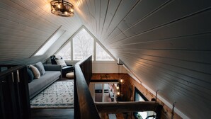 A cozy loft bedroom with a sloped ceiling, a wooden staircase, a sofa, and a view of the outdoors. - Secluded Rustic-Modern Log Cabin w/ Hot Tub, Private Creekside Escape (Ferryville)