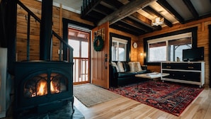 A cozy living room with a fireplace, wooden walls, a sofa, a coffee table, and a TV. - Secluded Rustic-Modern Log Cabin w/ Hot Tub, Private Creekside Escape (Ferryville)