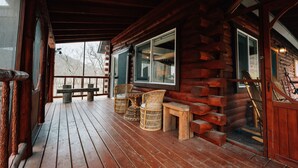 A wooden cabin with a porch, wicker chairs, a bench, and a staircase leading inside. - Secluded Rustic-Modern Log Cabin w/ Hot Tub, Private Creekside Escape (Ferryville)
