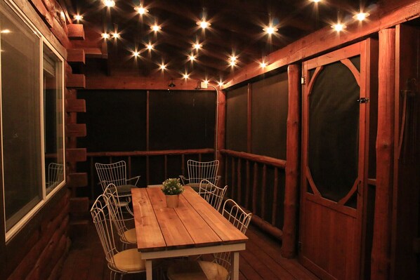 A wooden deck with a table and chairs, surrounded by walls with large windows and a door. - Secluded Rustic-Modern Log Cabin w/ Hot Tub, Private Creekside Escape (Ferryville)