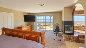 Ein Schlafzimmer mit einem großen Bett, einem Fernseher, einem Schreibtisch und Blick ins Freie.