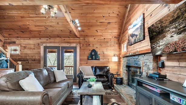 A cozy cabin interior with a leather sofa, a coffee table, a fireplace, and wooden walls.