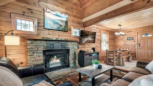 A cozy log cabin interior with a stone fireplace, leather sofas, and wooden walls.
