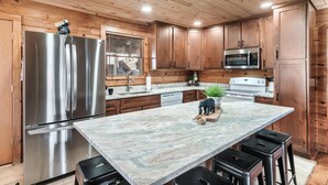 A modern kitchen with wooden cabinets, stainless steel appliances, and a marble countertop.